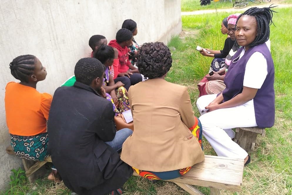 Nurse Carole sitting among a group of people during a community outreach, Zambia